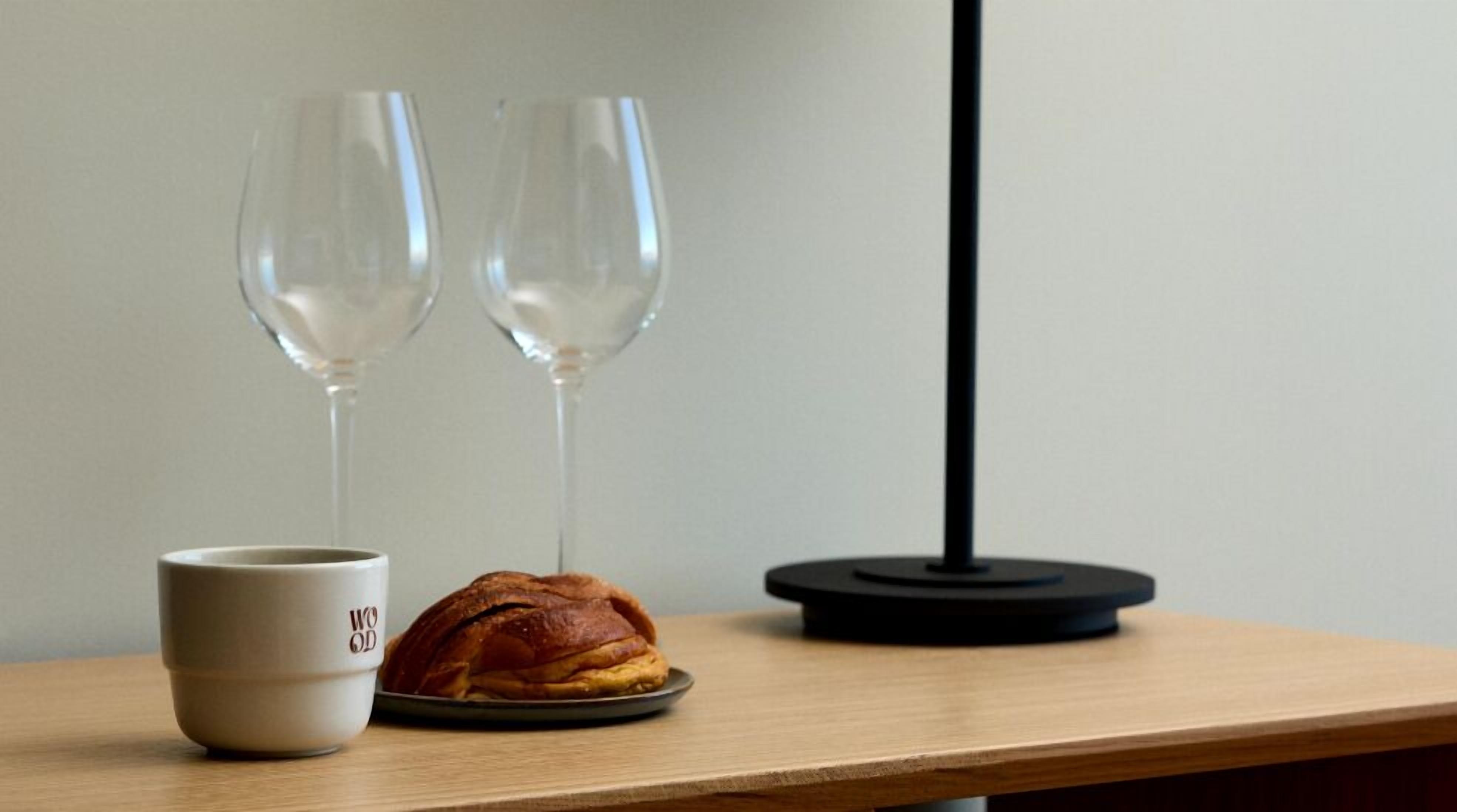 A wooden table with a white mug labeled "WOOD," a croissant, and two wine glasses.