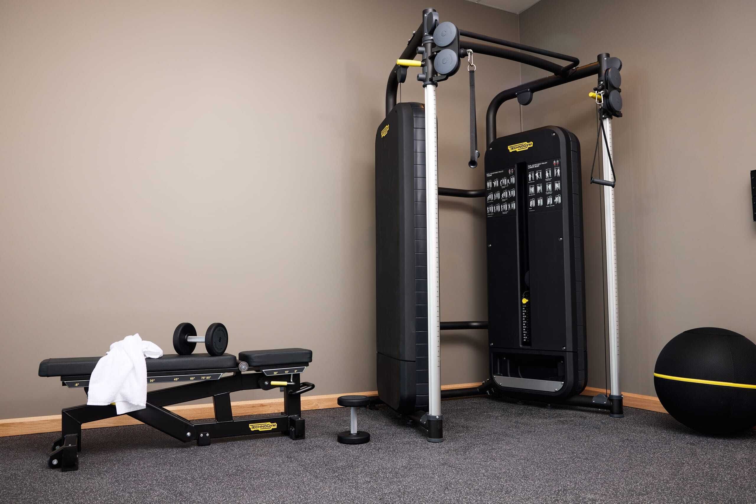 A gym with a bench, weight machine, and exercise ball.
