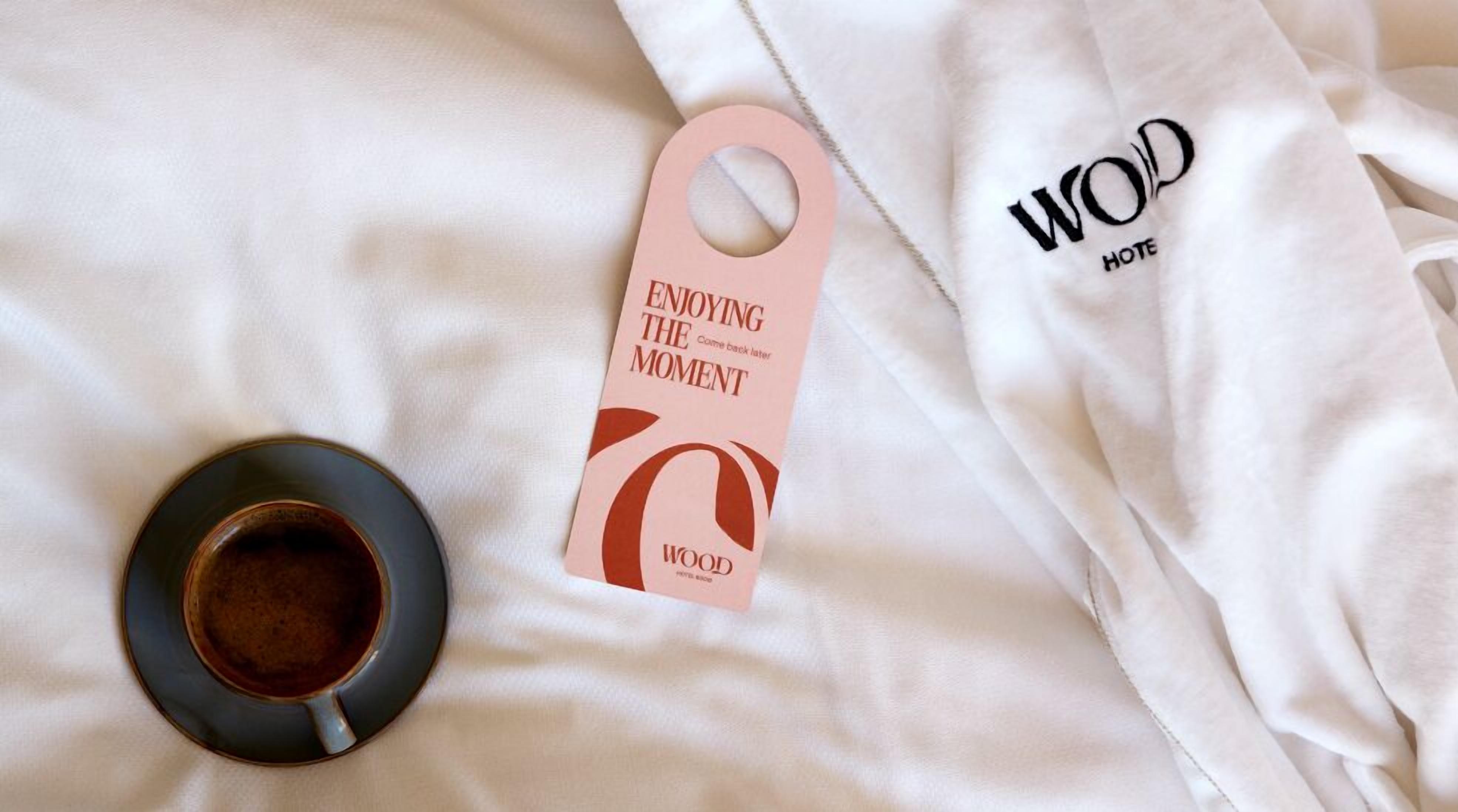 A bed with a white sheet, a tag with 'ENJOYING THE MOMENT' text, and a cup of coffee.