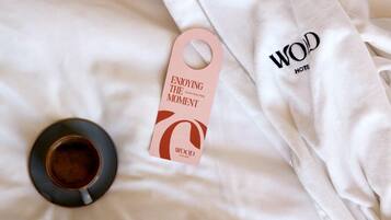A bed with a white sheet, a tag with 'ENJOYING THE MOMENT' text, and a cup of coffee.