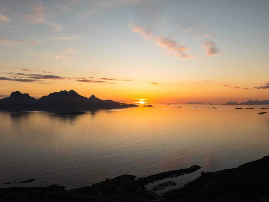 Una puesta de sol tranquila sobre un cuerpo de agua en calma, con montañas a lo lejos.