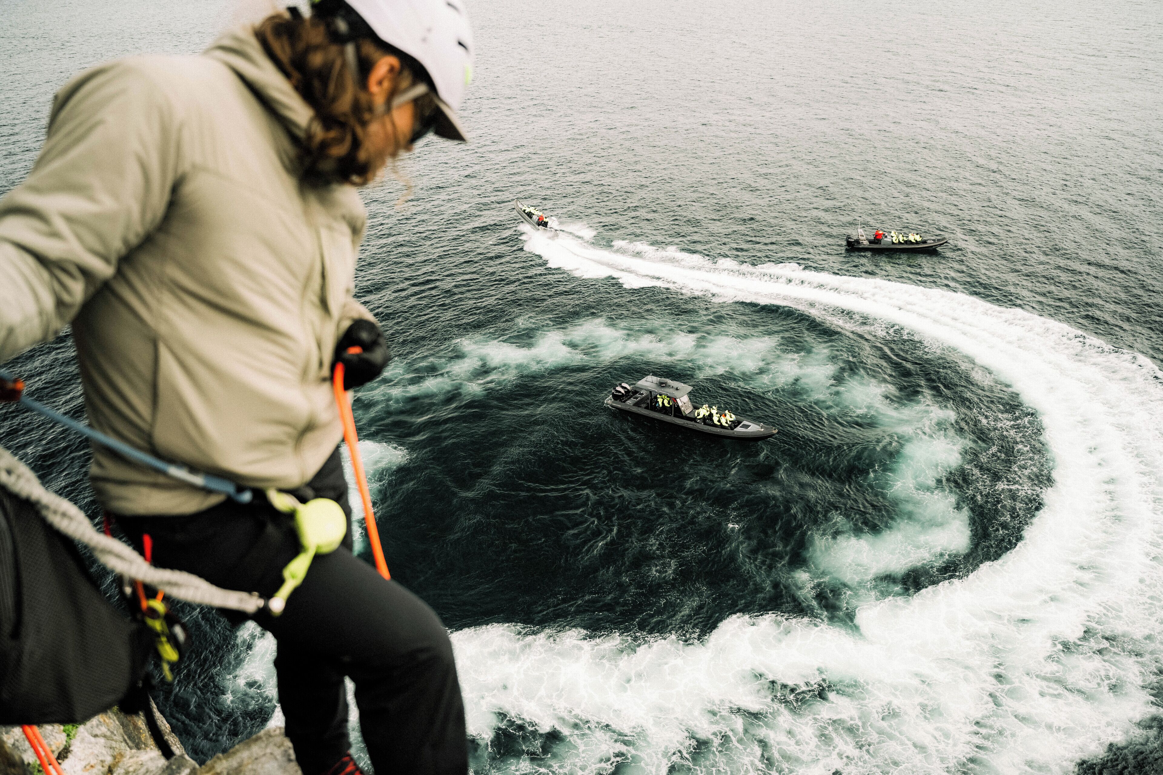 Eine Person auf einem Boot, beobachtet ein anderes Boot, das eine Bugwelle im Wasser hinterlässt.
