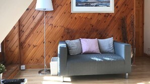 A room with a wooden sloped ceiling, a grey sofa with cushions, a floor lamp, and a framed picture on the wall. - STYLISH APARTMENT WITH PRIVATE ROOF TERRACE (Edinburgh)