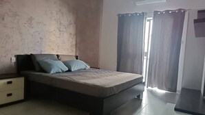 Une chambre à coucher avec un lit, une table de chevet, une commode et une fenêtre avec des rideaux.