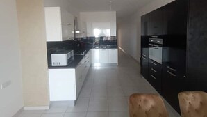 Une cuisine moderne avec des meubles blancs, un plan de travail noir et un coin repas agrémenté d’une chaise marron.