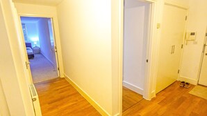 Ein Flur mit Holzdielen, weißen Wänden und einer Tür, die in ein Schlafzimmer mit Bett und Nachttisch führt.