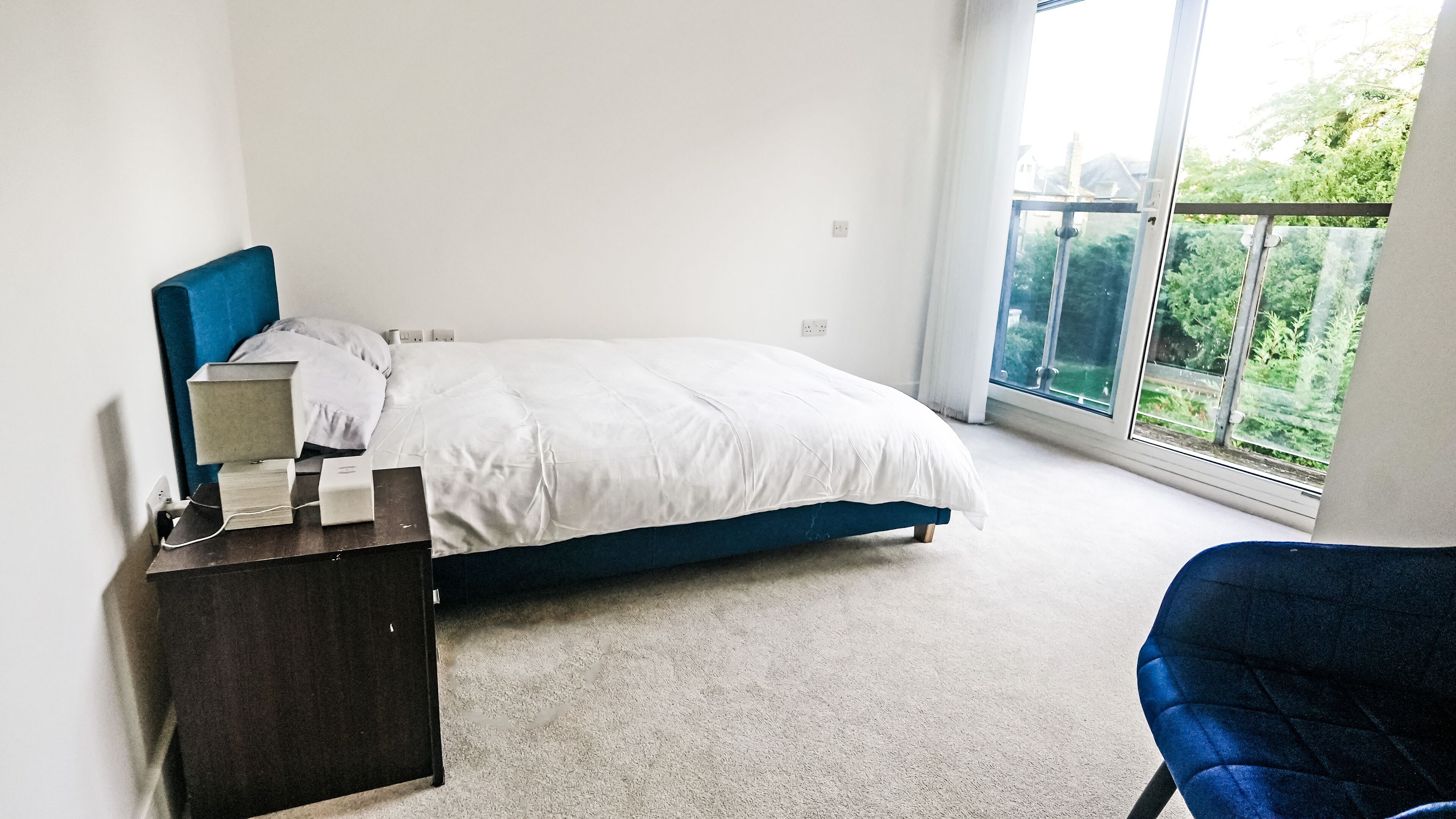 Une chambre à coucher comprenant un lit, une table de chevet, une chaise et une grande fenêtre donnant sur un paysage verdoyant.