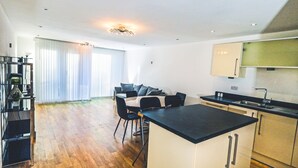 Eine moderne Küche mit einer zentralen Kochinsel, einem Essbereich mit Sofa und Stühlen sowie einem großen Fenster mit Jalousien.
