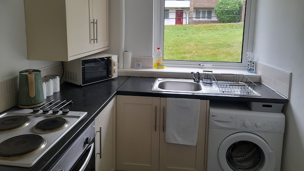 Een compacte keuken met een ingebouwde oven, magnetron, spoelbak en wasmachine.