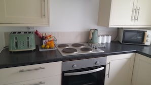 Een keuken met een broodrooster, waterkoker, magnetron en kookplaat. Er zijn kastjes, een aanrecht en een spoelbak.