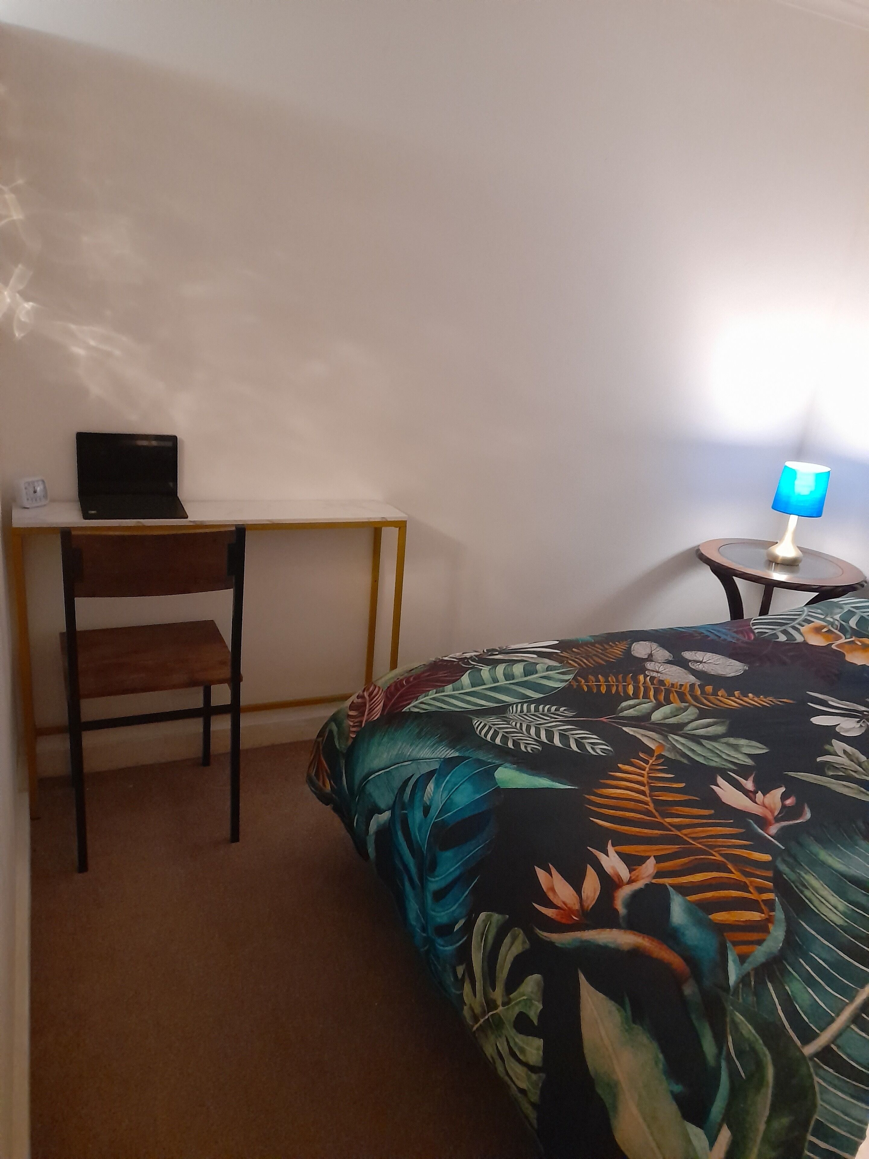 A room with a bed, a desk, a chair, and a small table with a lamp.