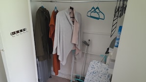 Een kleine, smalle kamer met een kast vol hangende kleding en enkele planken.