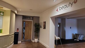 Un couloir avec une pancarte indiquant « beauté », une porte en bois, une plante en pot et une chaise blanche.