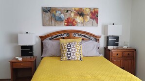 Ein ordentlich bezogenes Bett mit einer gelben Steppdecke, zwei Nachttische mit Lampen und einem floralen Bild darüber.