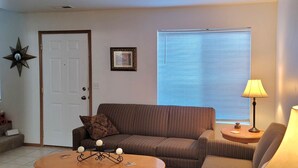 Ein Wohnzimmer mit einem gestreiften Sofa, einem runden Couchtisch, einer Lampe, einer Stern-Dekoration, einem gerahmten Bild und einem Fenster mit Jalousien.
