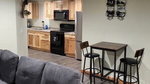 Een moderne keuken met houten kastjes, een zwarte magnetron en een roestvrijstalen koelkast. Er is een eethoek met een tafel en twee stoelen.
