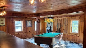 Een pooltafel in een ruimte met houten wanden en plafond, een bar en een neonreclame.