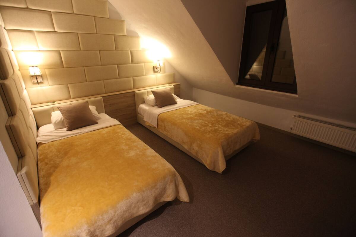 A twin bedroom with two beds, a headboard with built-in lighting, a window, and a radiator.