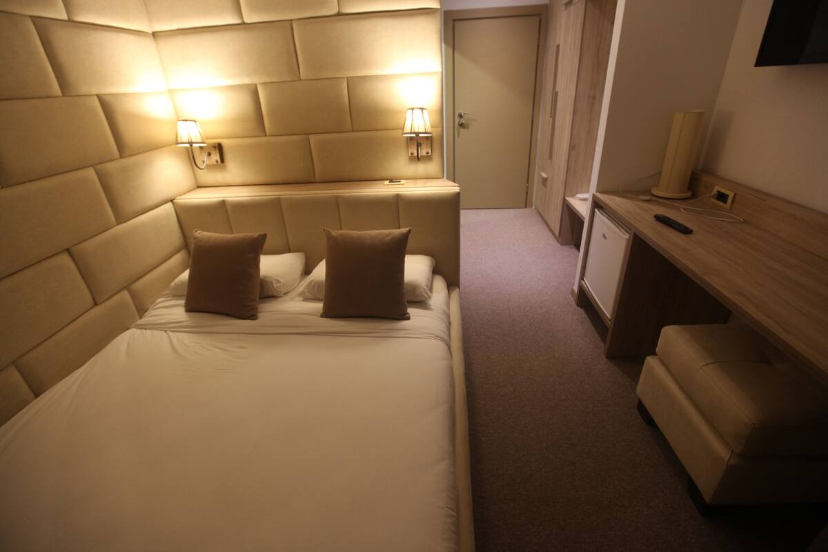 A hotel room with a large bed, two bedside lamps, a small desk, and a door.