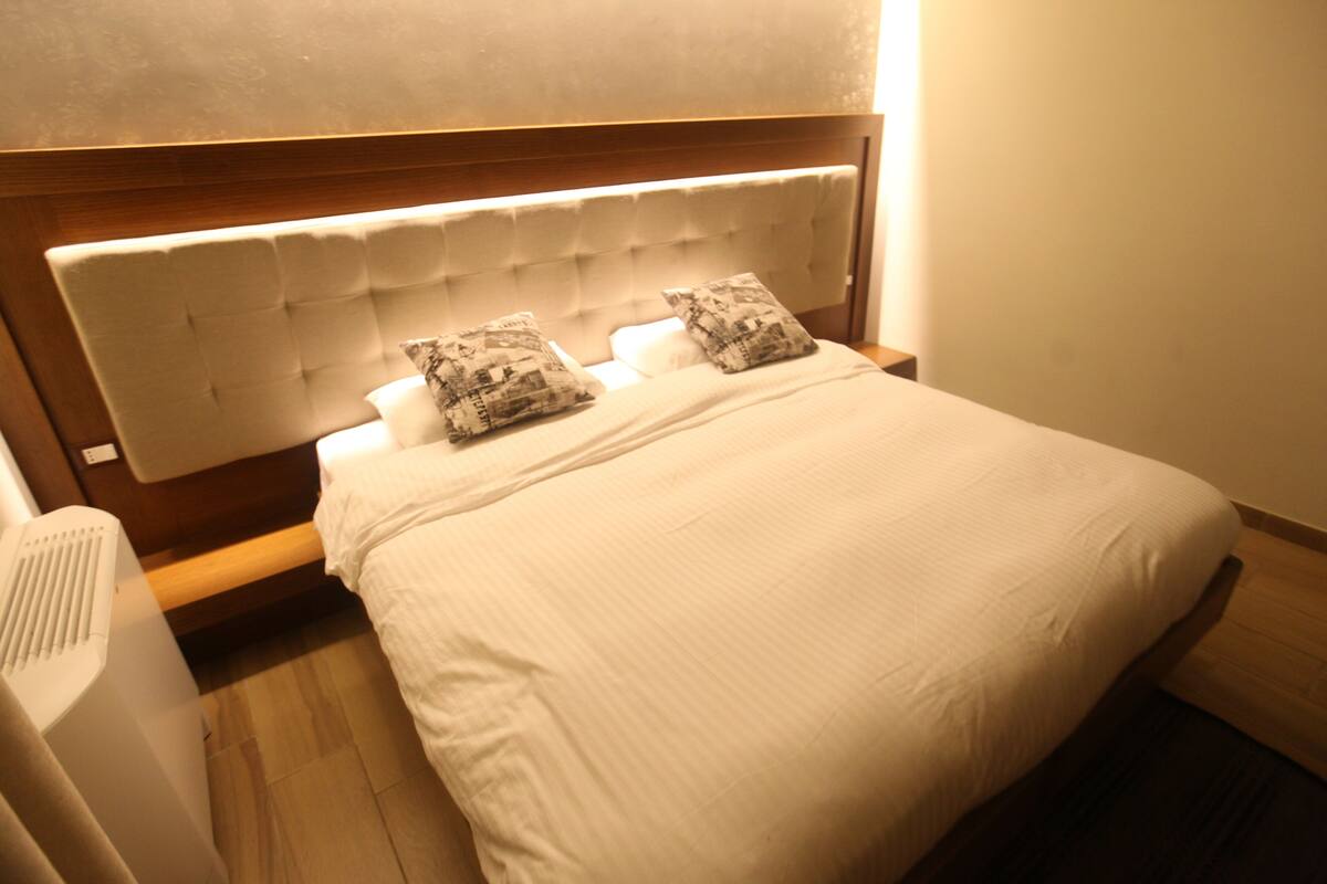 A neatly made bed with a tufted headboard, two patterned pillows, and a white comforter.
