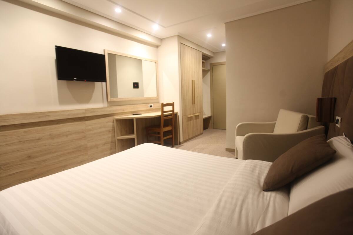 A hotel room with a bed, a desk, a chair, a television, and a wardrobe.