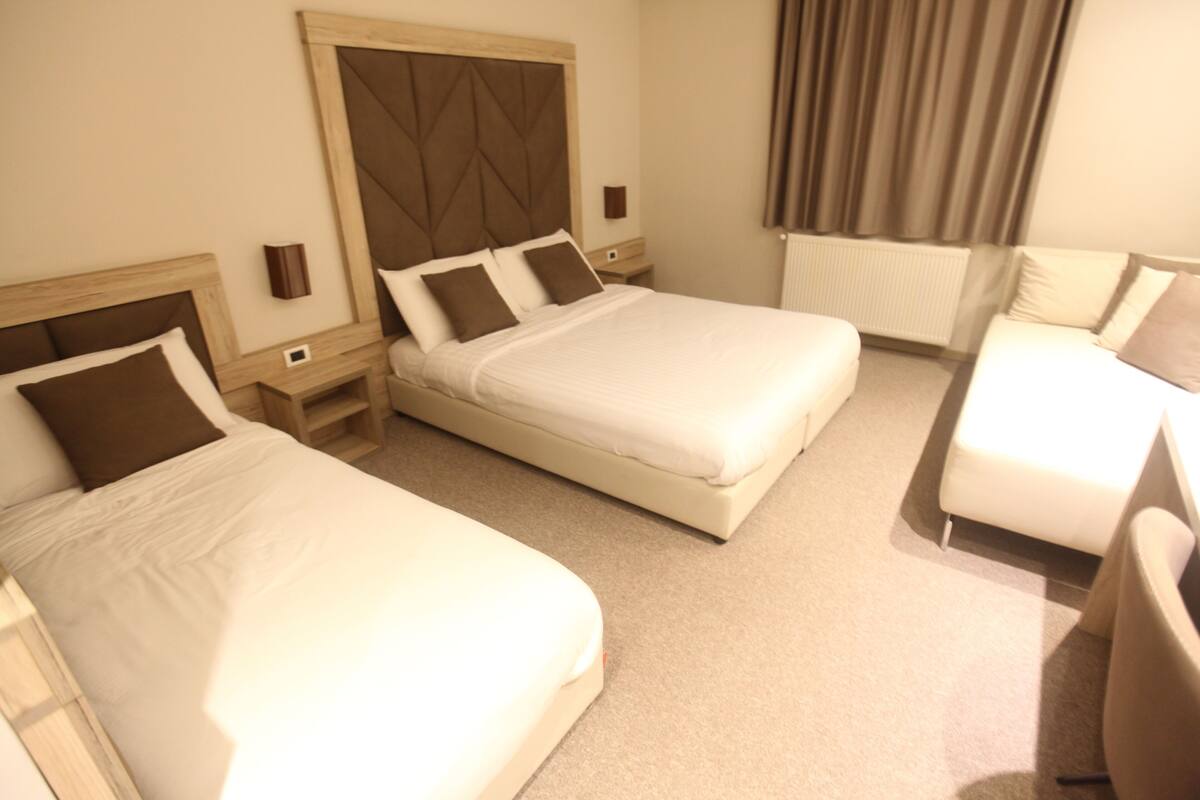 A hotel room with two beds, a sofa, and a small table.