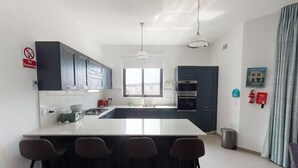 Une cuisine moderne dotée d’un îlot central, de tabourets de bar, de meubles de couleur sombre et d’appareils électroménagers en acier inoxydable.