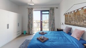 Une chambre dotée d’un grand lit, d’une armoire, d’un balcon avec des rideaux et offrant une vue sur la ville.