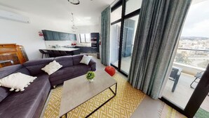 Un salon moderne avec un canapé, une table basse et une vue sur la ville grâce à de grandes fenêtres.