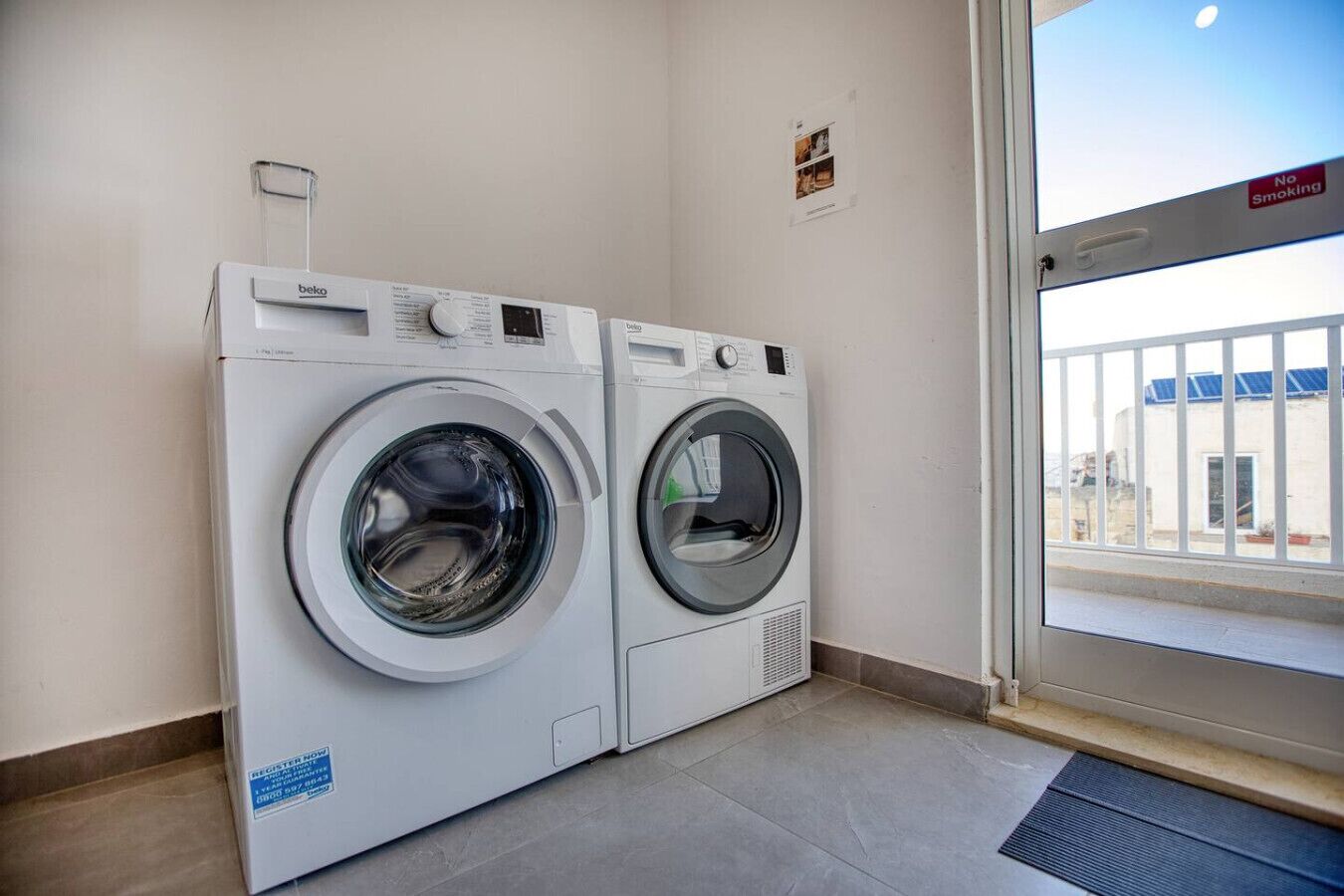 Une buanderie équipée de deux machines à laver à chargement frontal, d’un panneau «Il est interdit de fumer» et offrant une vue sur un bâtiment à l’extérieur.