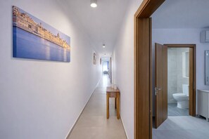 A hotel hallway with a painting of a cityscape, a wooden bench, and a bathroom visible through an open door. - Modern 3-bedroom apartment Pieta (Tal-Pietà)