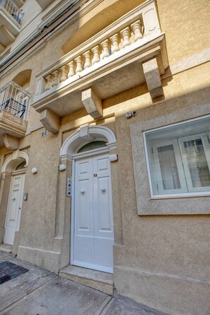 Un bâtiment avec une porte blanche, un balcon doté de balustrades et une fenêtre.