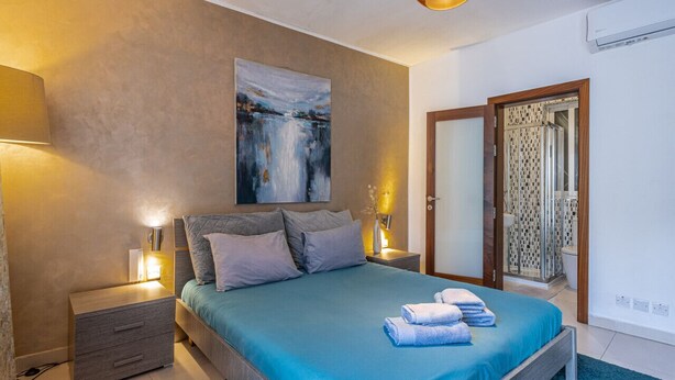 Un dormitorio con cama, mesitas de noche, un cuadro y la puerta del baño.