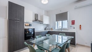 Una cocina moderna con una mesa de comedor de vidrio, armarios grises y un horno empotrado.