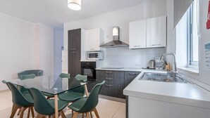 Una cocina moderna con armarios blancos, una mesa de comedor de vidrio y sillas verdes.