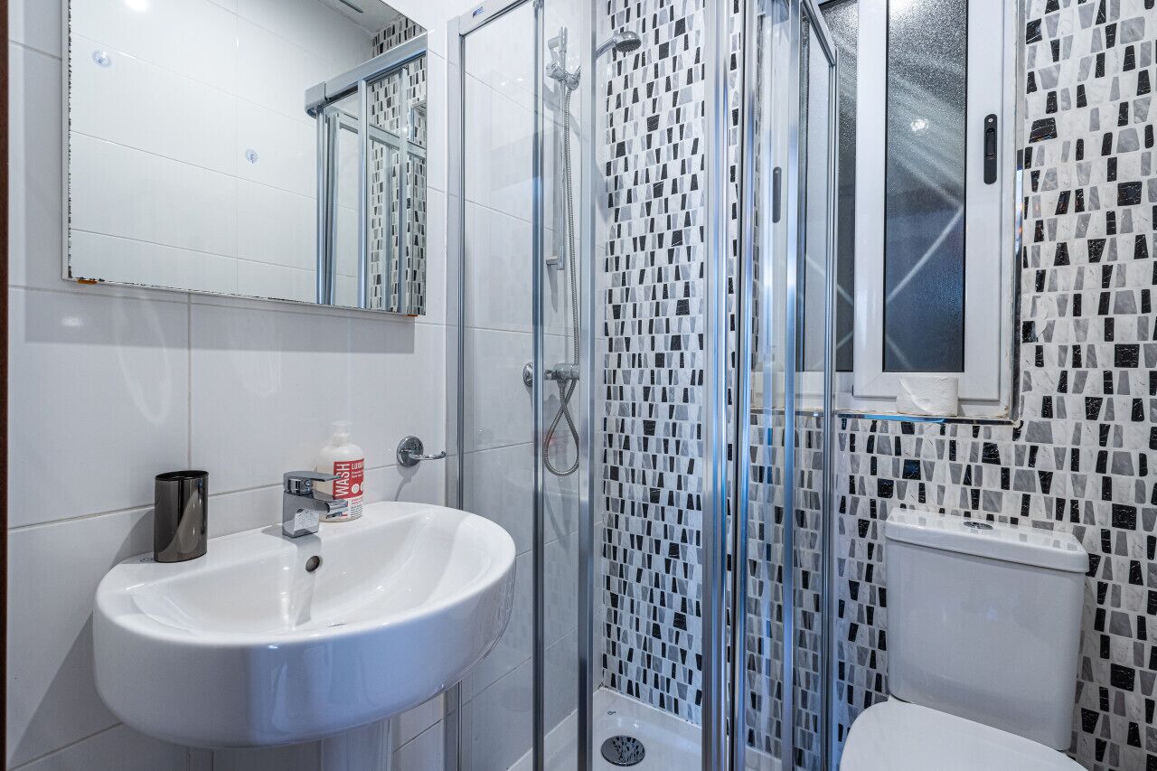 A bathroom with a white sink, a glass shower enclosure, and a mosaic-tiled wall.