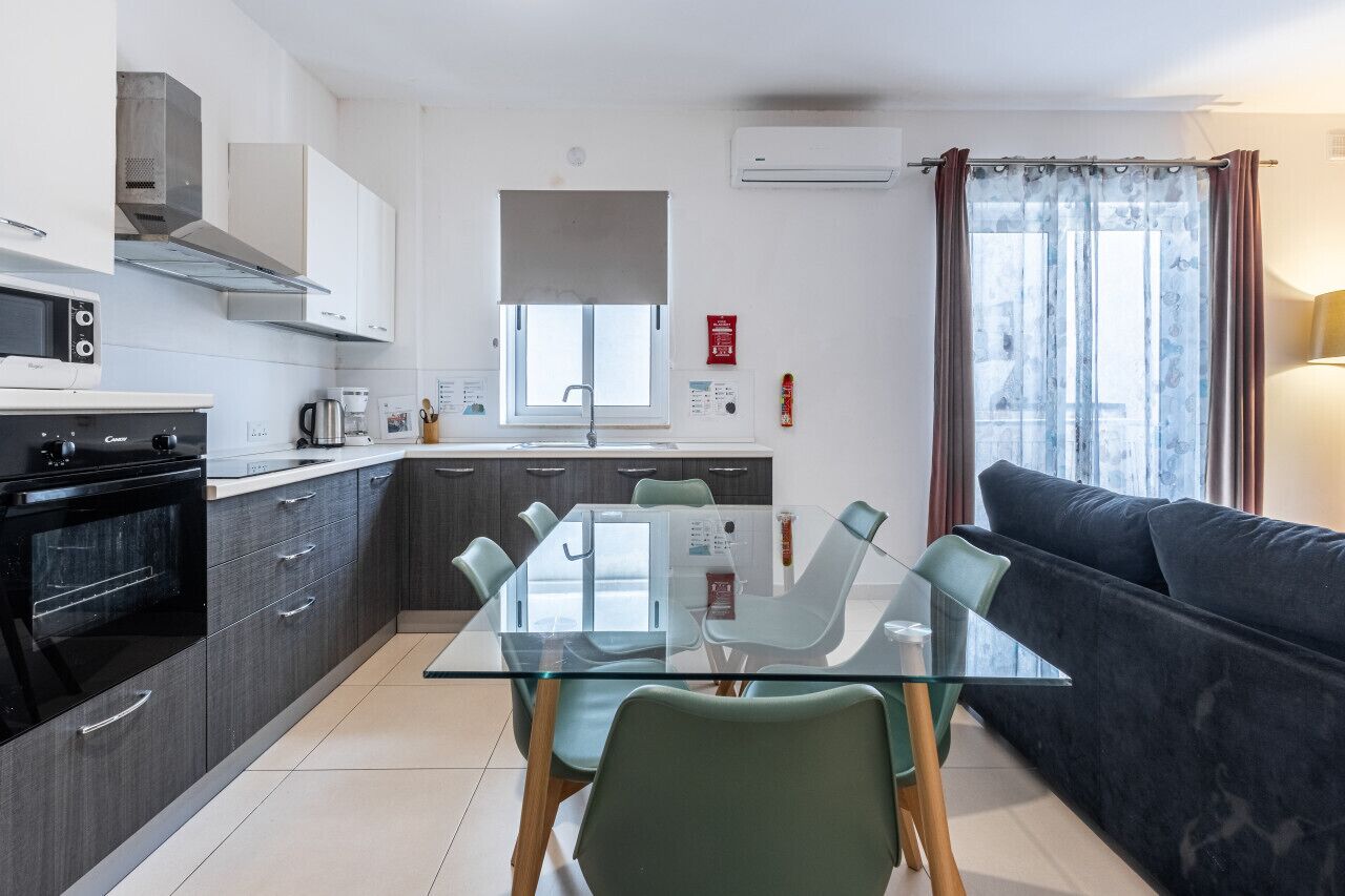 A modern kitchen with a dining table, chairs, a sofa, and a window with curtains.