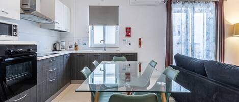 A modern kitchen with a dining table, chairs, a sofa, and a window with curtains.