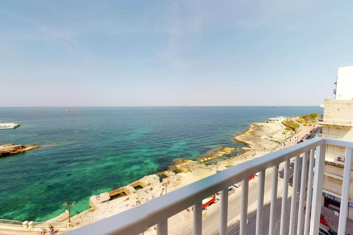 Vista sulla costa dal balcone, cielo sereno, costa rocciosa e mare calmo.