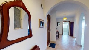 A hallway with a wooden-framed mirror, a door, and a view into another room with a tiled floor and a hanging light fixture. - 6th floor seafront apartment with open sea views. (Tas-Sliema)