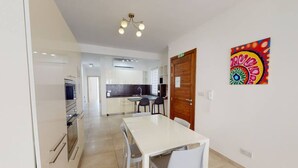 A modern kitchen with white cabinets, a dining table with chairs, and a colorful artwork on the wall. - Modern 2-bedroom apartment in Gzira (Il-Gżira)