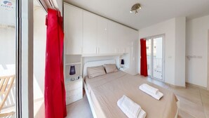 A modern bedroom with a large bed, a nightstand, a lamp, and a sliding glass door to a balcony. - Modern 2-bedroom apartment in Gzira (Il-Gżira)