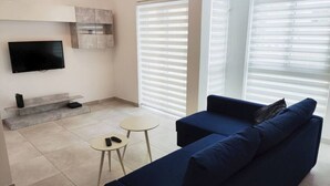 A modern living room with a dark blue sofa, a flat-screen TV mounted on the wall, a small round table, and a built-in shelf. - Modern 2-bedroom apartment in Gzira (Il-Gżira)