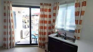 A small kitchen with a sink and cabinets, a sliding glass door leading to an outdoor area, and curtains with a geometric pattern. - Modern 5th floor 2 bedroom apartment in Tigne (Sliema)