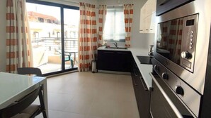 A compact kitchen with a built-in oven and a dining area with a table and chairs. - Modern 5th floor 2 bedroom apartment in Tigne (Sliema)