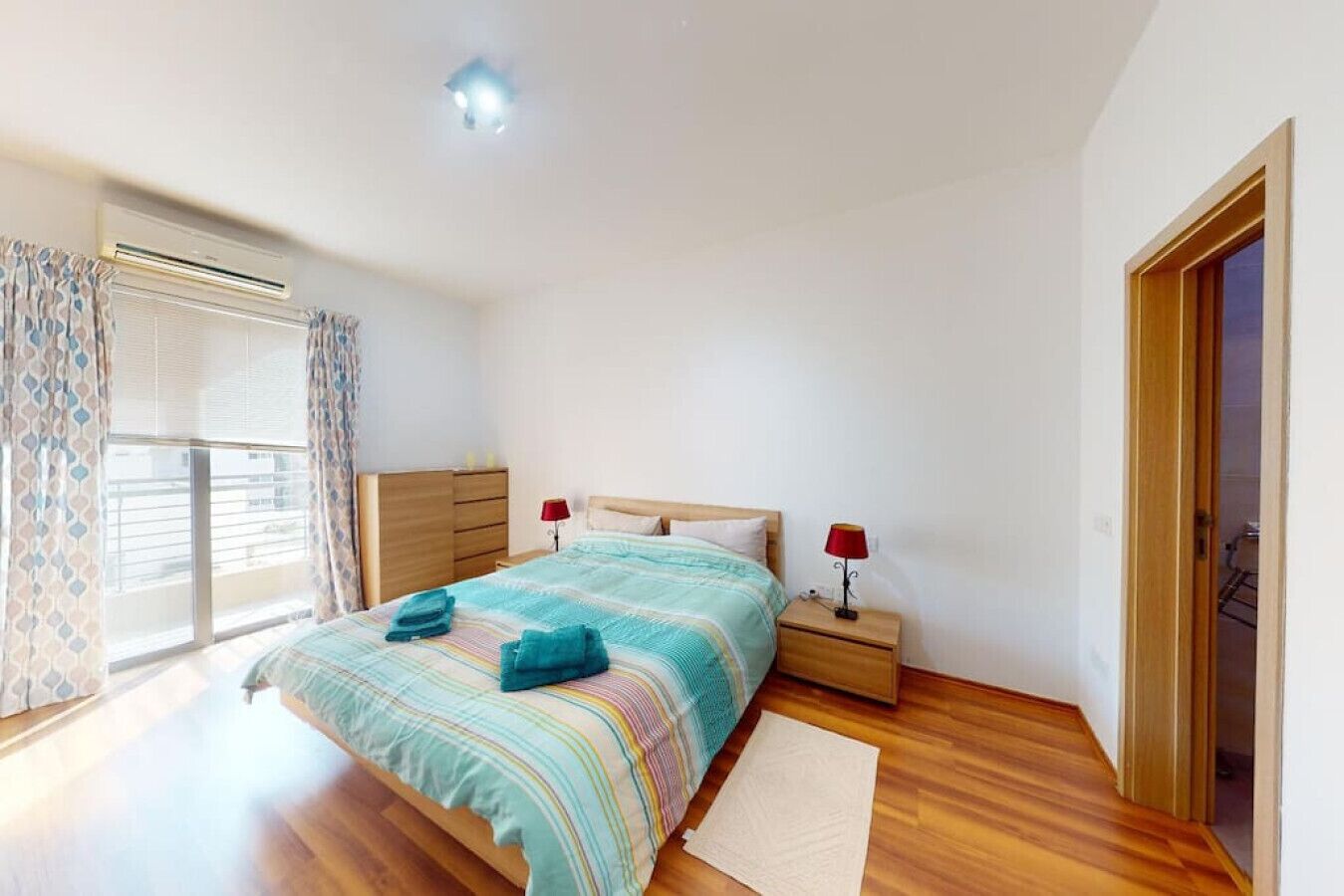 Een slaapkamer met een bed, nachtkastjes, een houten kledingkast, een raam met gordijnen en een deur.