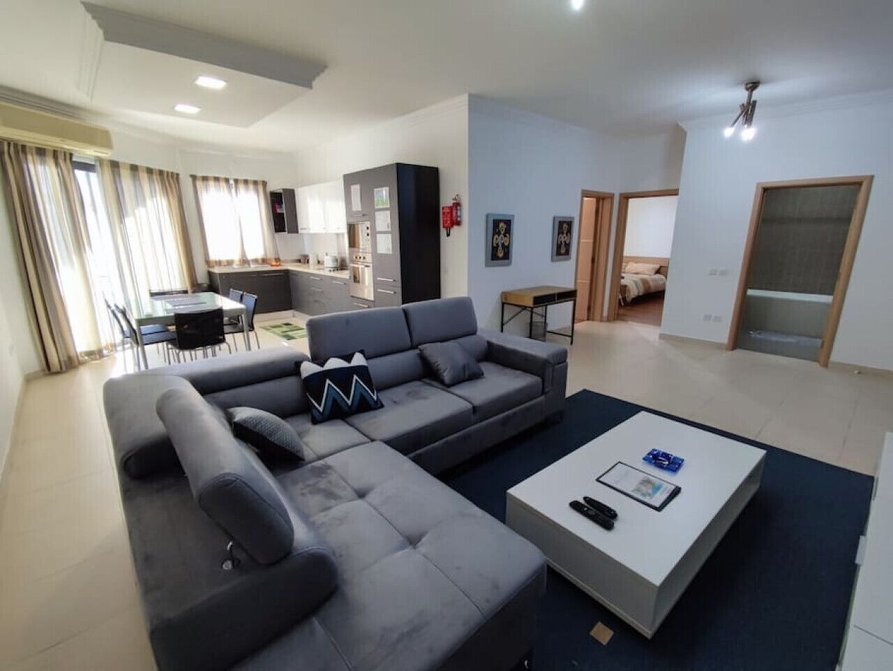 Ein modernes Wohnzimmer mit einem grauen Ecksofa, einem weißen Couchtisch und einem Essbereich im Hintergrund.