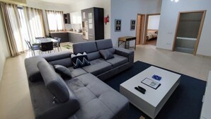 Ein modernes Wohnzimmer mit einem grauen Ecksofa, einem weißen Couchtisch und einem Essbereich im Hintergrund.
