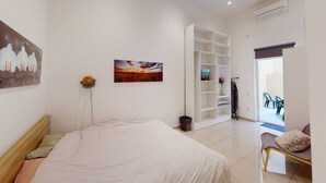 A bedroom with a bed, a white wardrobe, a painting, and a view of an outdoor area with chairs. - Spacious 3 bedroom maisonette (Tas-Sliema)