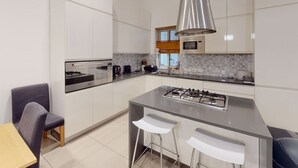 A modern kitchen with white cabinets, a stainless steel stove, a microwave, and a large pendant light. - Spacious 3 bedroom maisonette (Tas-Sliema)